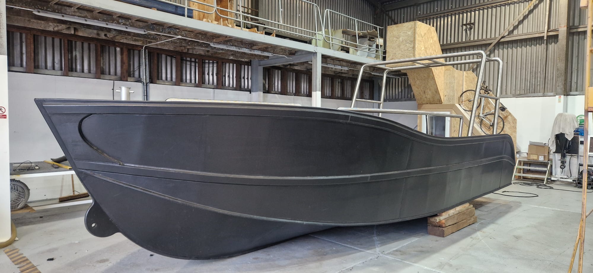 Port-side view of an unpainted HDPE workboat hull on pallets in the NESS Marine workshop, stainless steel roll bar fitted