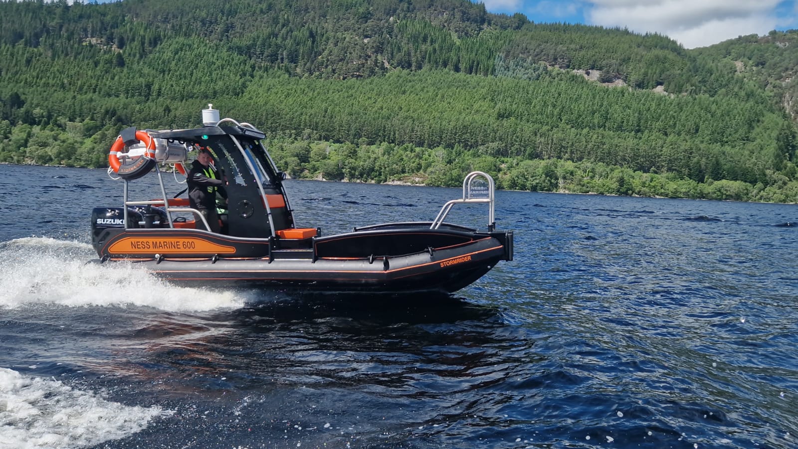 NESS Marine 600 Stormrider workboat running on Loch Ness with tree-lined bank behind